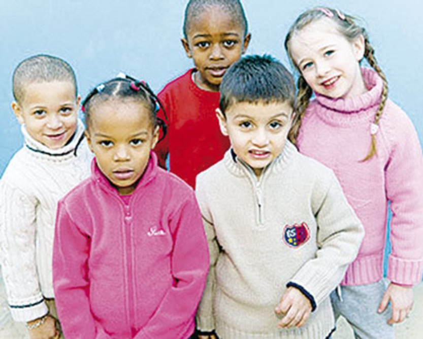 Five pre-school aged children standing together facing up to the camera. Most are smiling.
